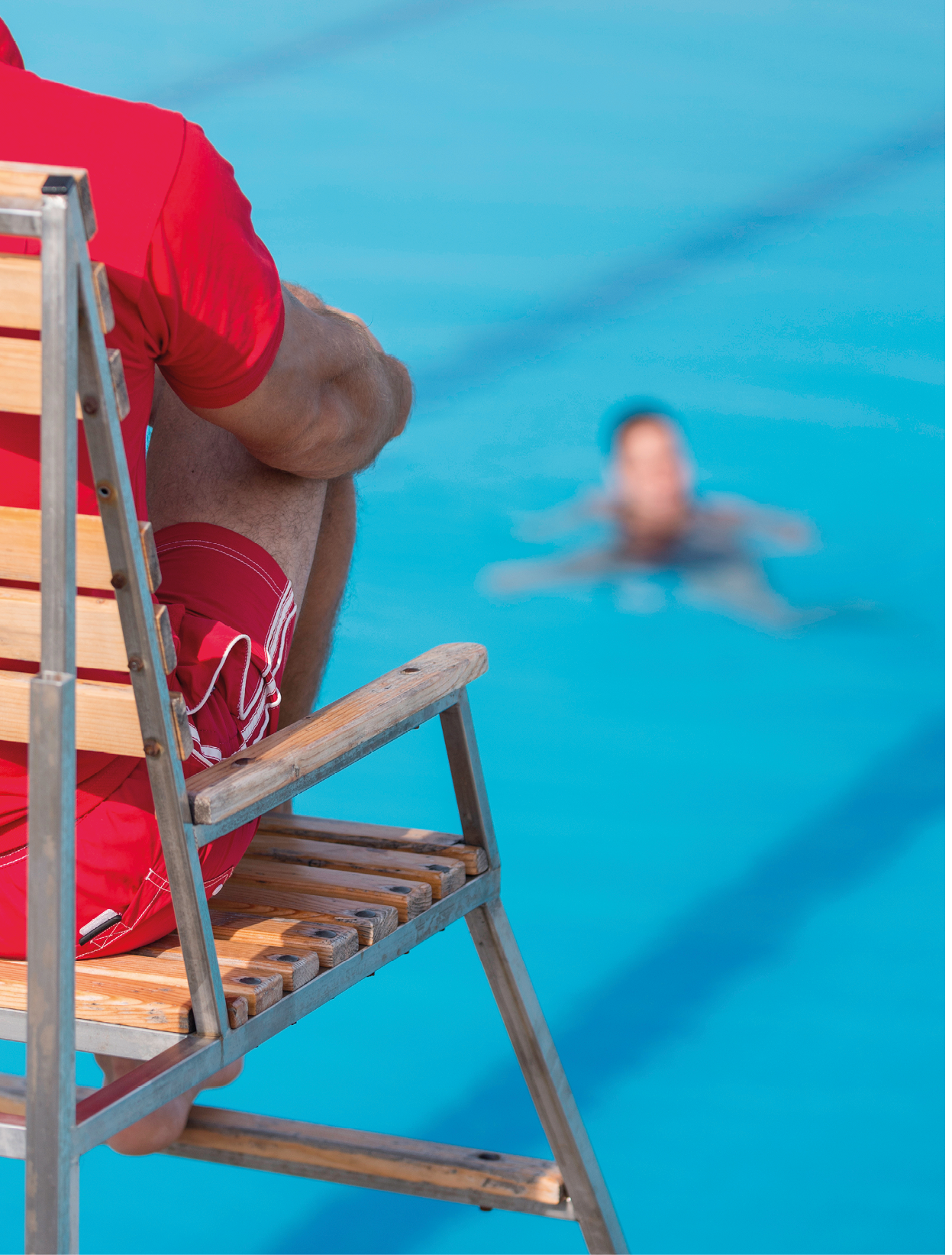Lifeguard on duty, sitting in chair above swimming pool